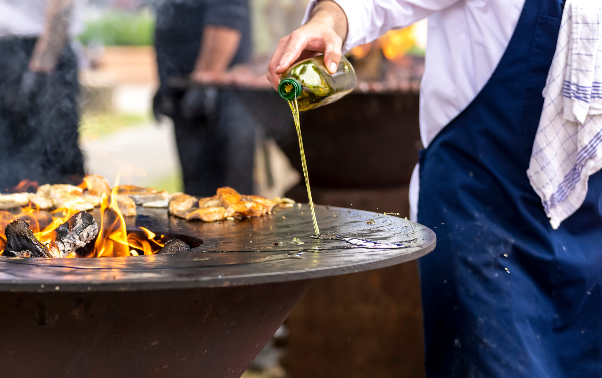 Roasting meat on a round barbecue with an open fire. The cook pours oil on the brazier